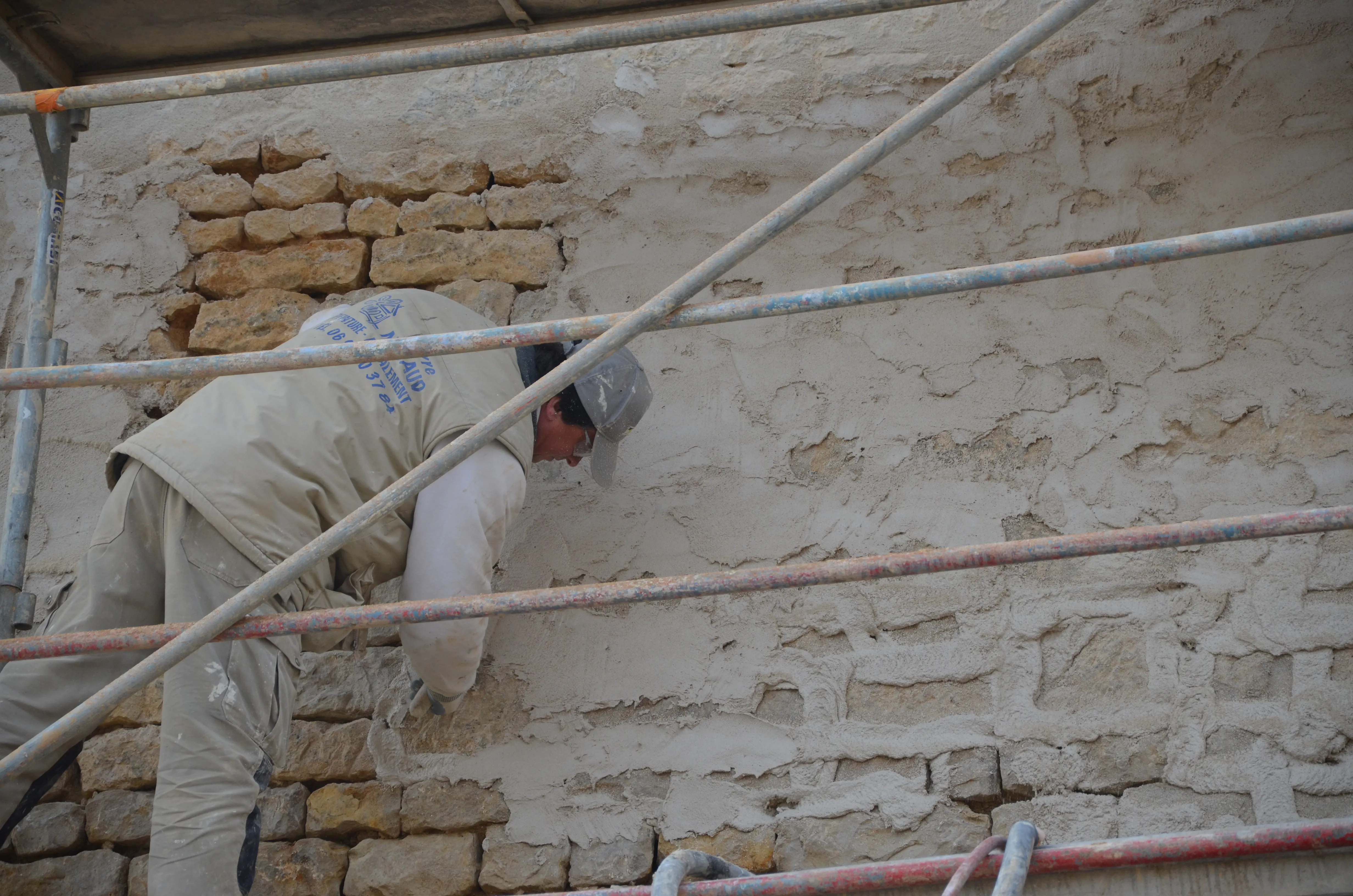Geste artisanal d'enduit frais écrasé à la truelle sur un mur de pierres